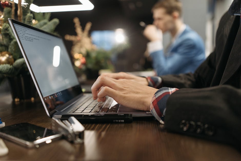 A professional man typing on a laptop in an elegant indoor office setting with a blurred background.